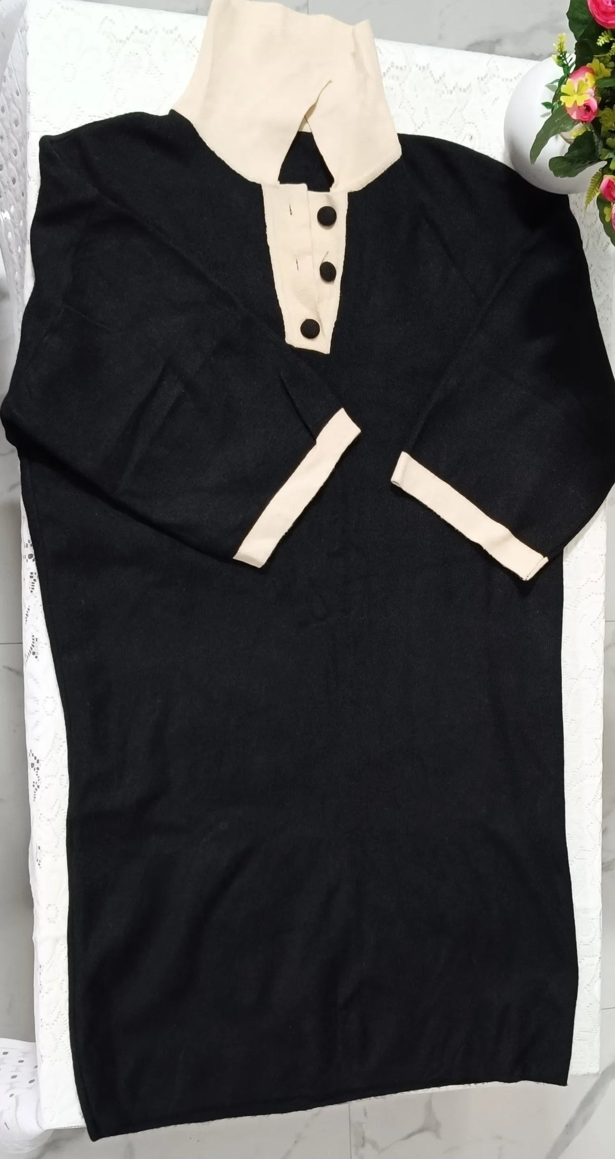 Black dress with beige collar and buttons on a marble surface with flowers.