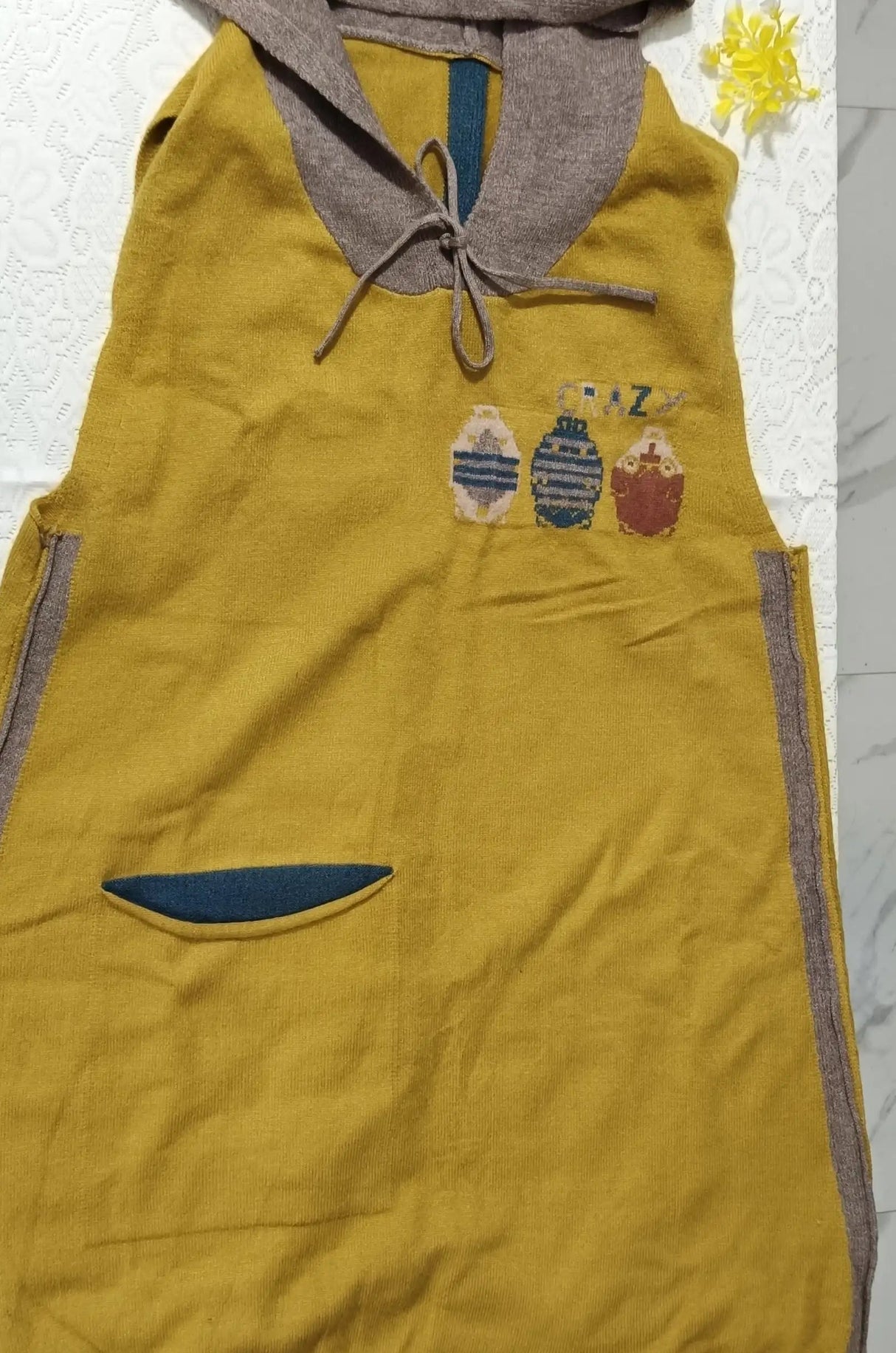 Yellow sleeveless hoodie with brown hood and colorful design on a marble surface