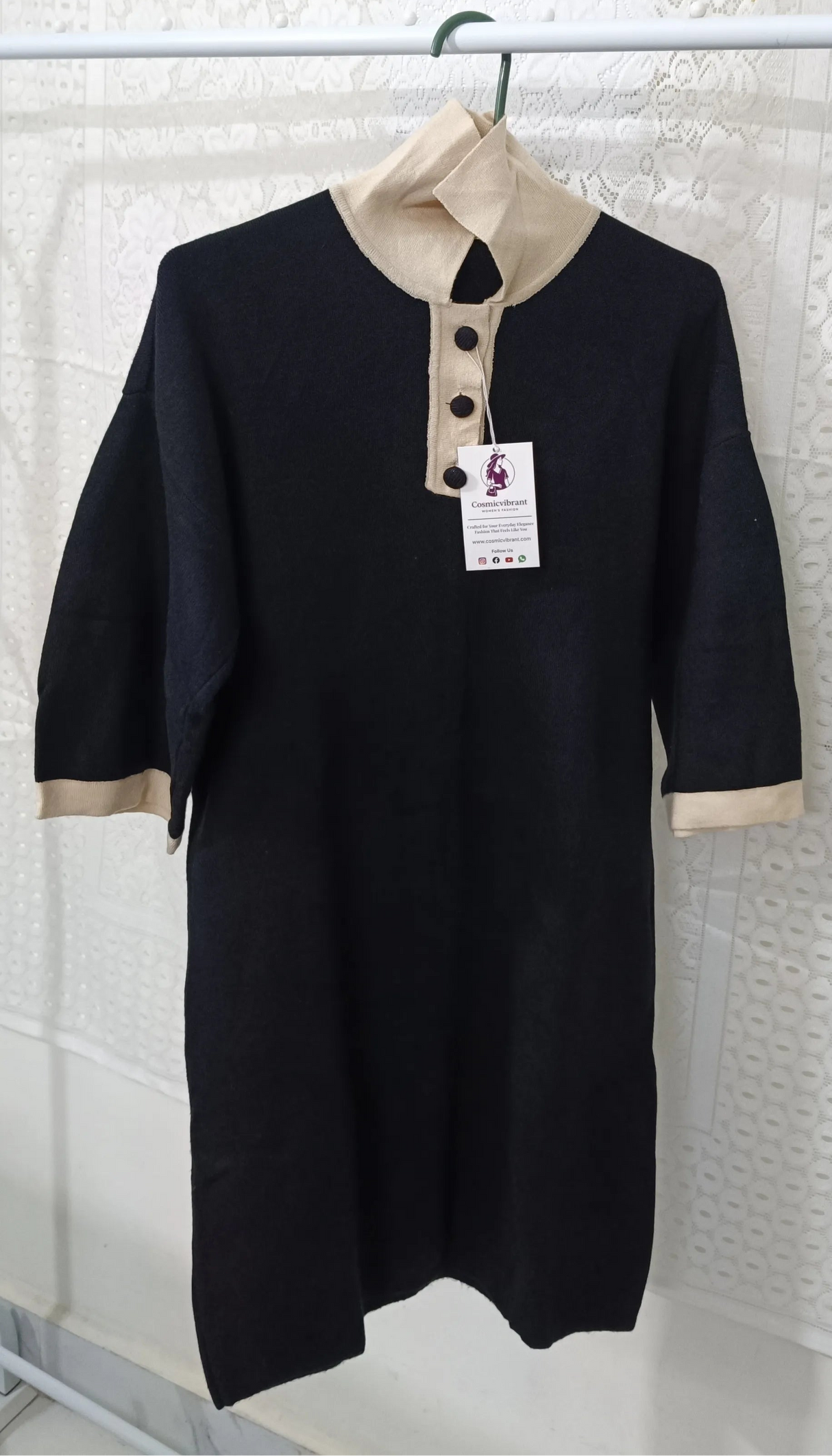 Black dress with beige trim on a hanger against a textured white wall