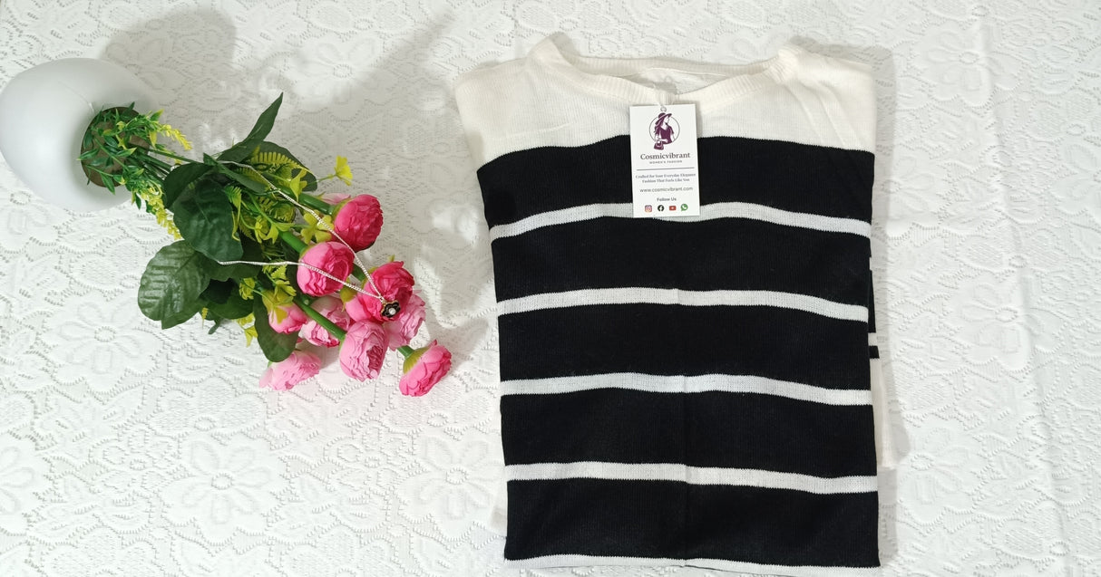 Black and white striped shirt with a tag on a textured white surface next to pink flowers.