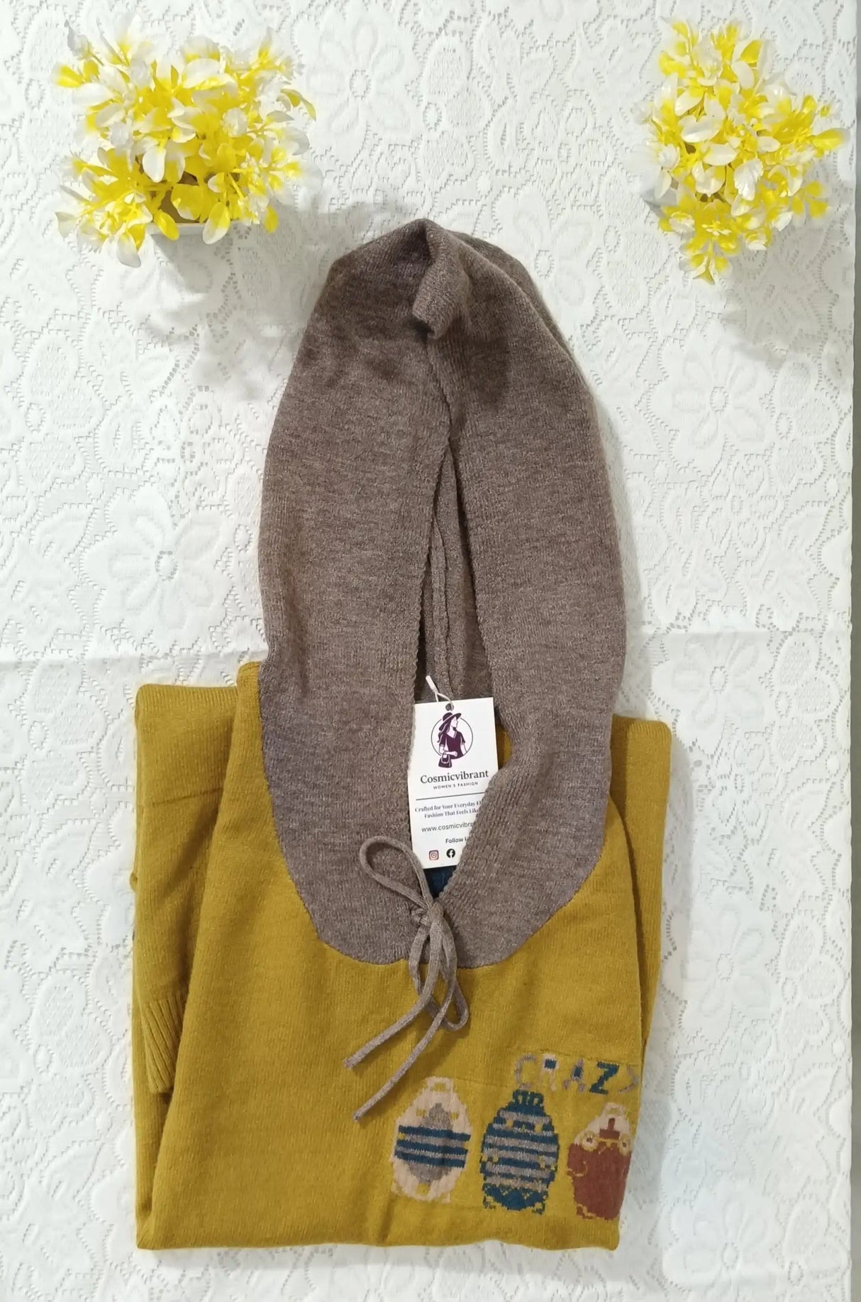 Folded yellow garment with a brown hat on top, against a textured white wall with yellow flowers.