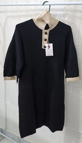 Black dress with beige trim on a hanger against a textured white wall