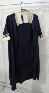 Navy dress with white collar and sleeves on a hanger against a textured white wall.