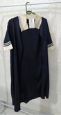 Navy dress with white collar and sleeves on a hanger against a textured white wall.