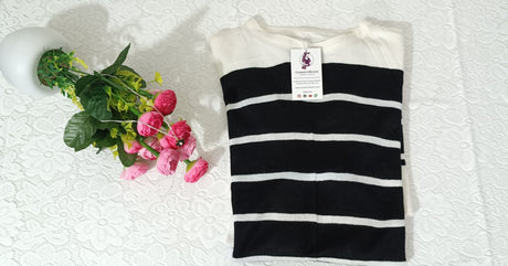 Black and white striped shirt with a tag on a textured white surface next to pink flowers.