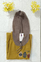 Folded yellow garment with a brown hat on top, against a textured white wall with yellow flowers.