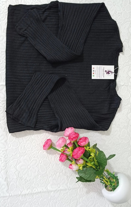 Black ribbed sweater with a tag on a white textured surface, accompanied by pink flowers.